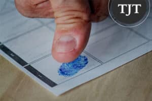 Person pressing an inked thumbprint onto a fingerprint card during booking in New Jersey
